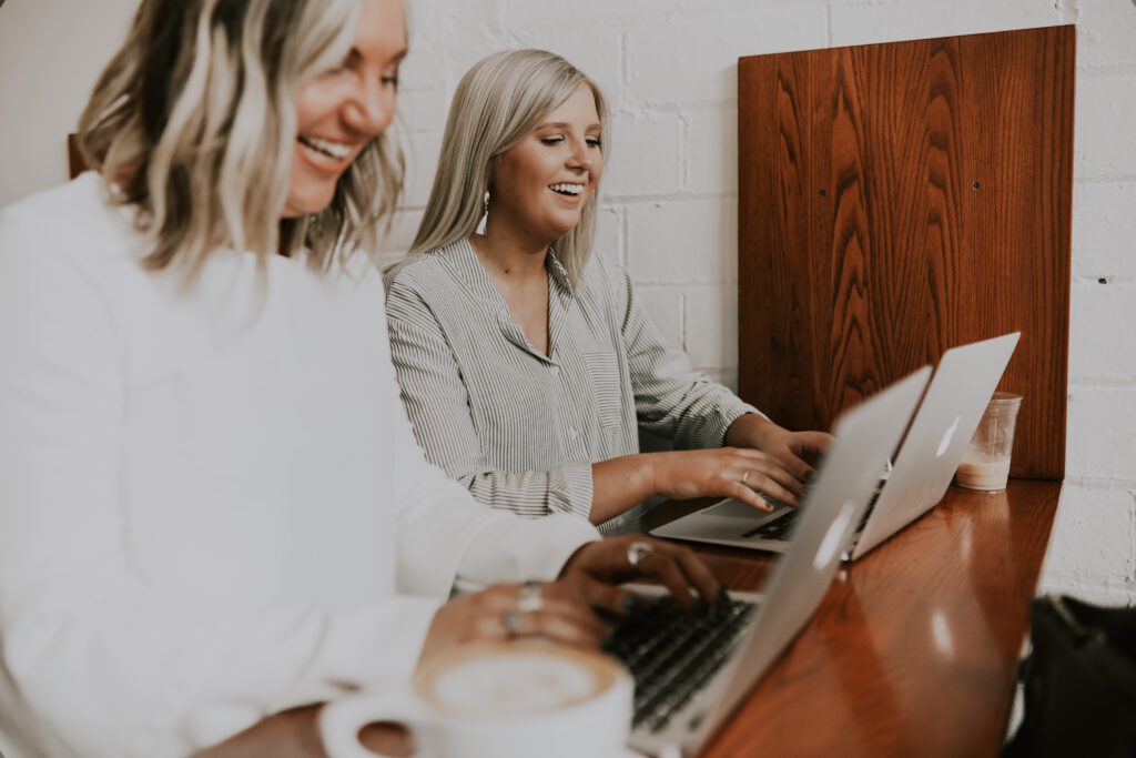 Two professional women laughing at their laptops playing games for remote teams.